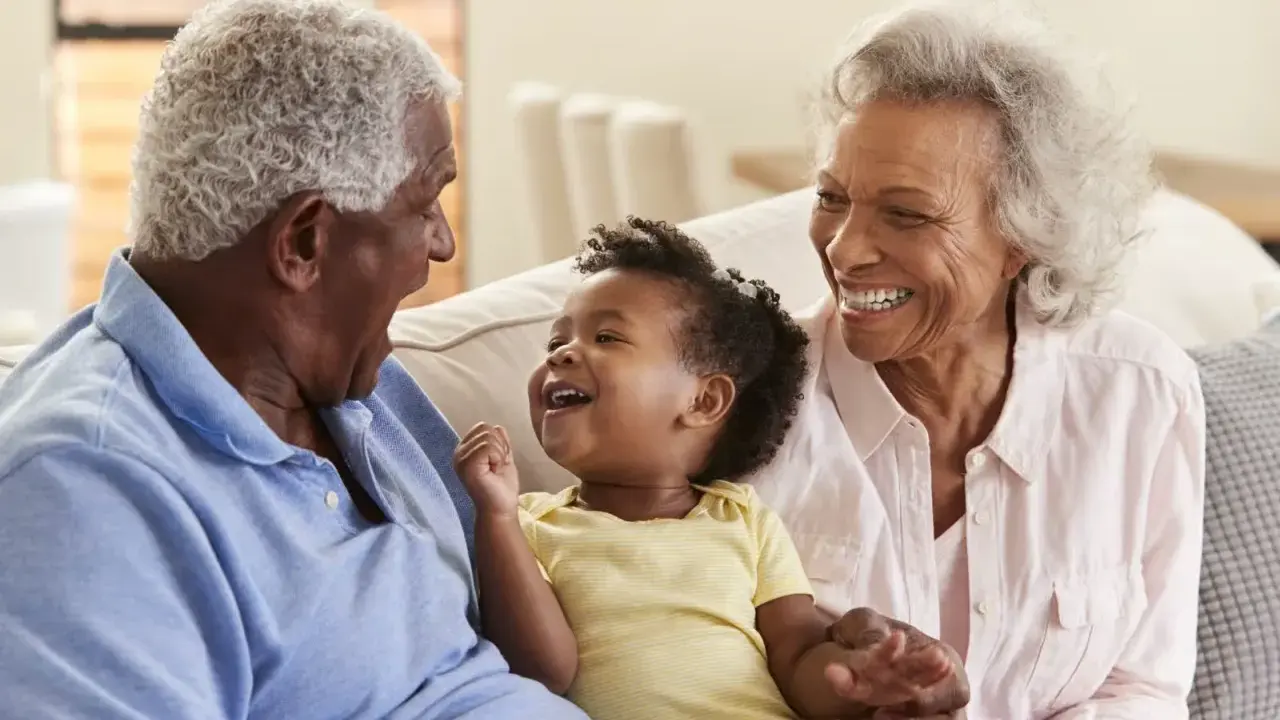 Un bébé rit aux éclats, entouré de ses grands-parents. La grand-mère, loin d'être indifférente, partage la joie de son petit-enfant.