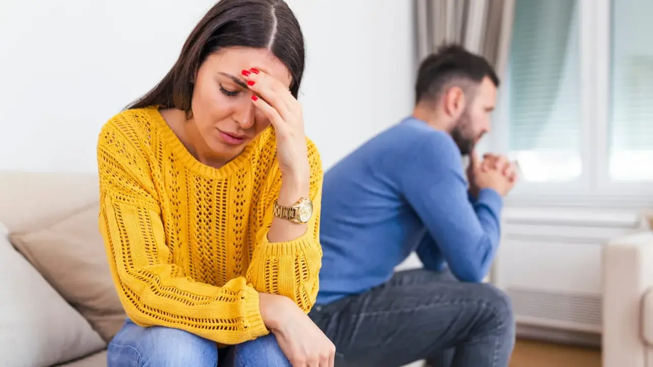 Une femme désemparée se tient la tête, son mari pensif est assis dos à elle. Elle se demande comment savoir si mon mari me trompe.