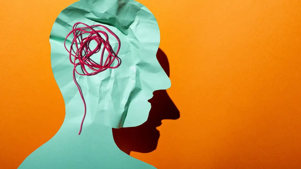 Silhouette d'une tête en papier froissé, avec un fil rouge emmêlé symbolisant la pensée complexe d'un esprit hpi neuroatypique.