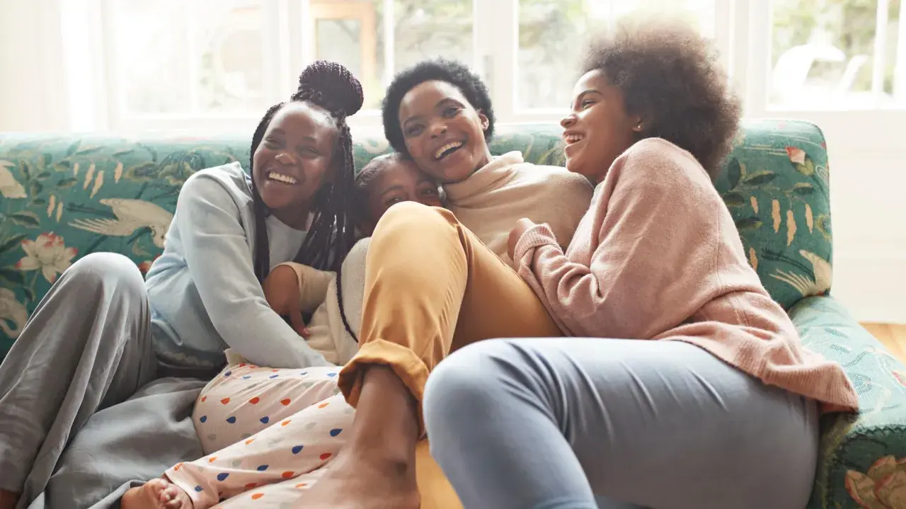 Une famille rit aux éclats sur un canapé. L'ainé de la famille, la plus grande, est au centre, entourée de ses sœurs.