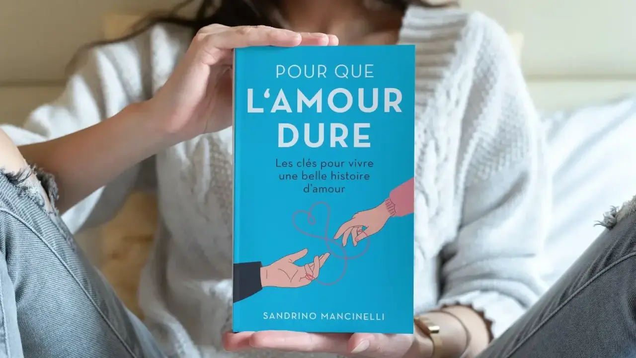 Un livre bleu intitulé "Pour que l'amour dure" est tenu par une personne. L'illustration montre deux mains se tendant l'une vers l'autre, symbolisant le début d'une histoire d'amour.