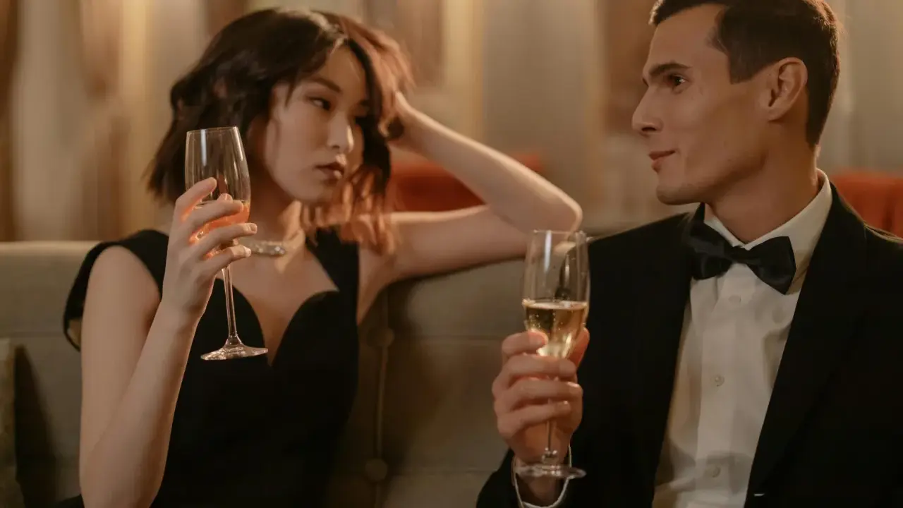 Un homme en smoking et une femme en robe noire sirotent du champagne, une scène qui pourrait inspirer sur comment séduire une fille.