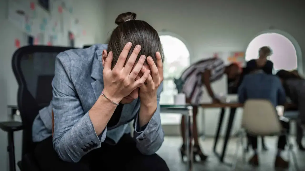 Personse tenant la tête entre les mains, visiblement stressée. Un test d'anxiété sociale pourrait révéler son état.