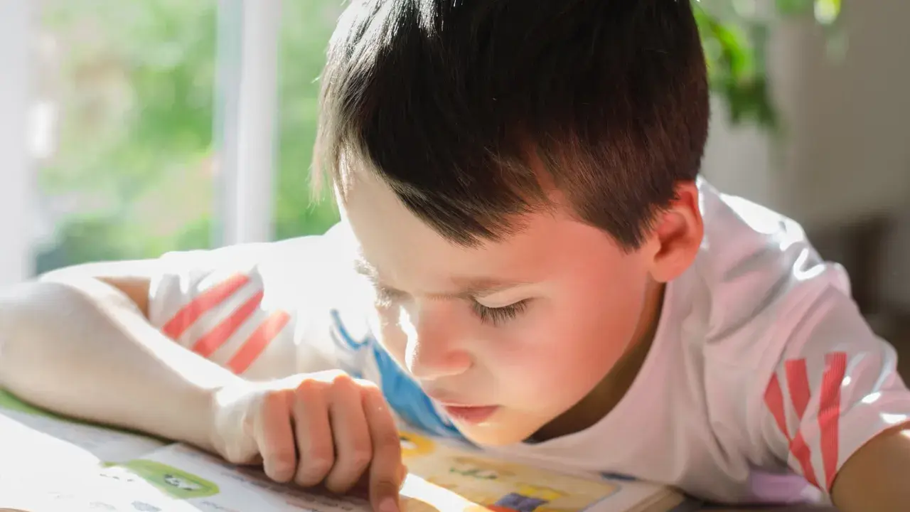 Un garçon concentré lit un livre, son doigt suivant les mots. Un test dys peut être un défi, mais sa détermination est claire.
