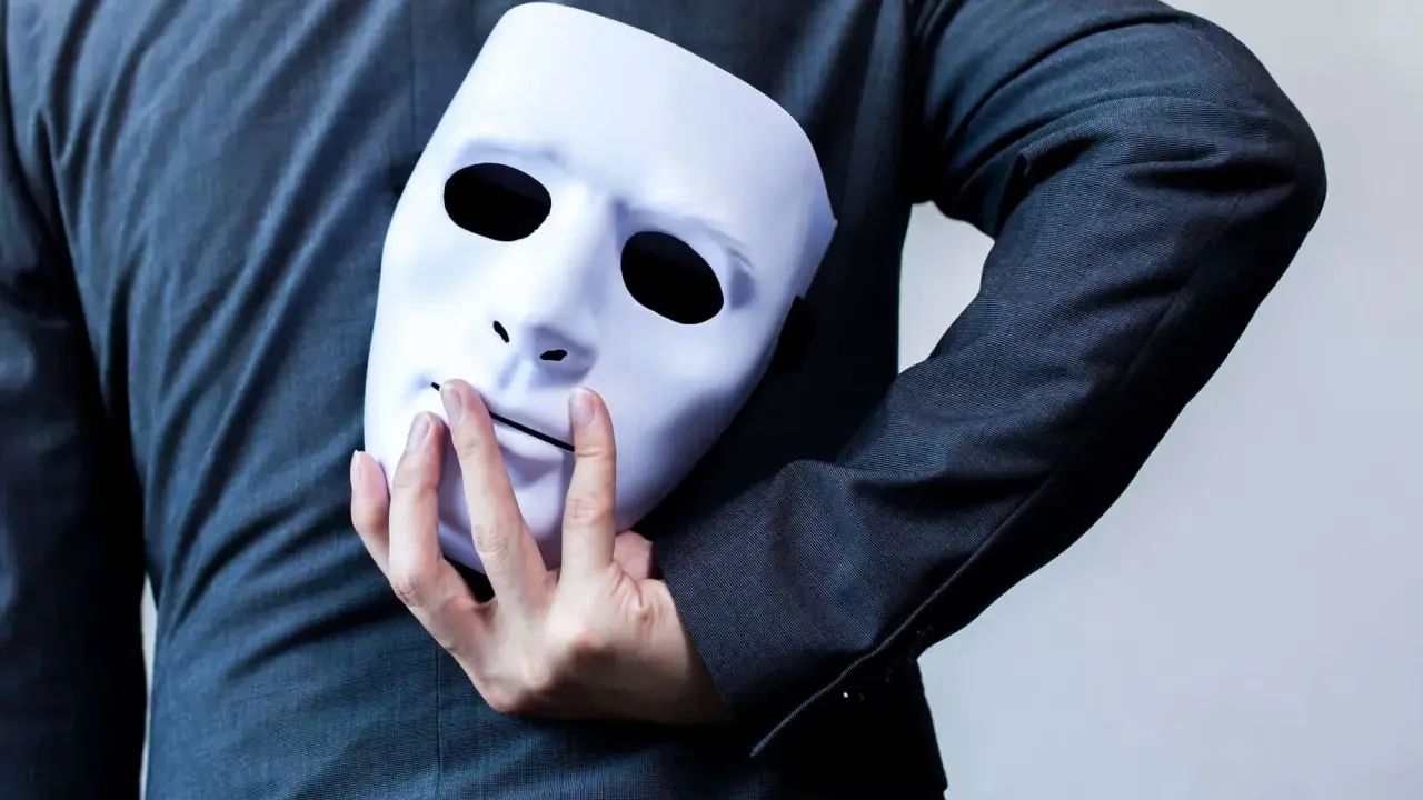 Une main cache un masque blanc derrière un costume. "Je suis narcissique, que faire ?" se demande la personne.