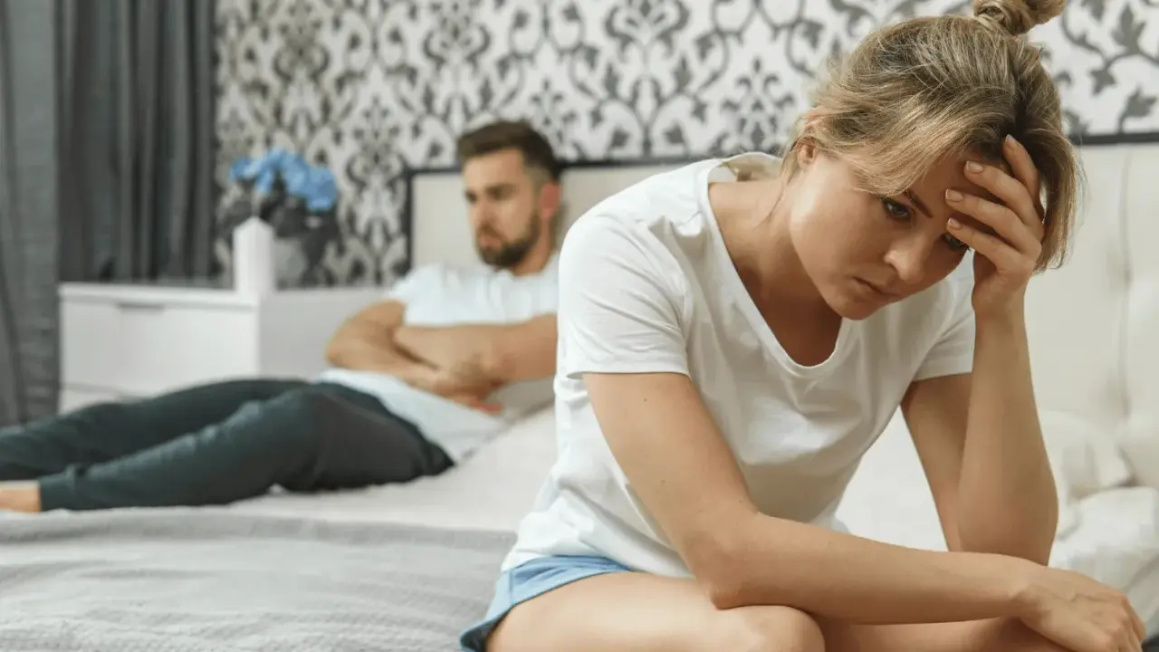 Une femme trompe son mari. Elle est assise sur le lit, la tête dans les mains, le regard perdu. Son mari, dos à elle, semble en colère.