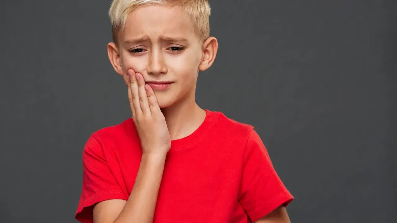 Un jeune garçon blond, le visage crispé, se tient la joue. Il semble triste, comme si mon fils se sent mal aimé.