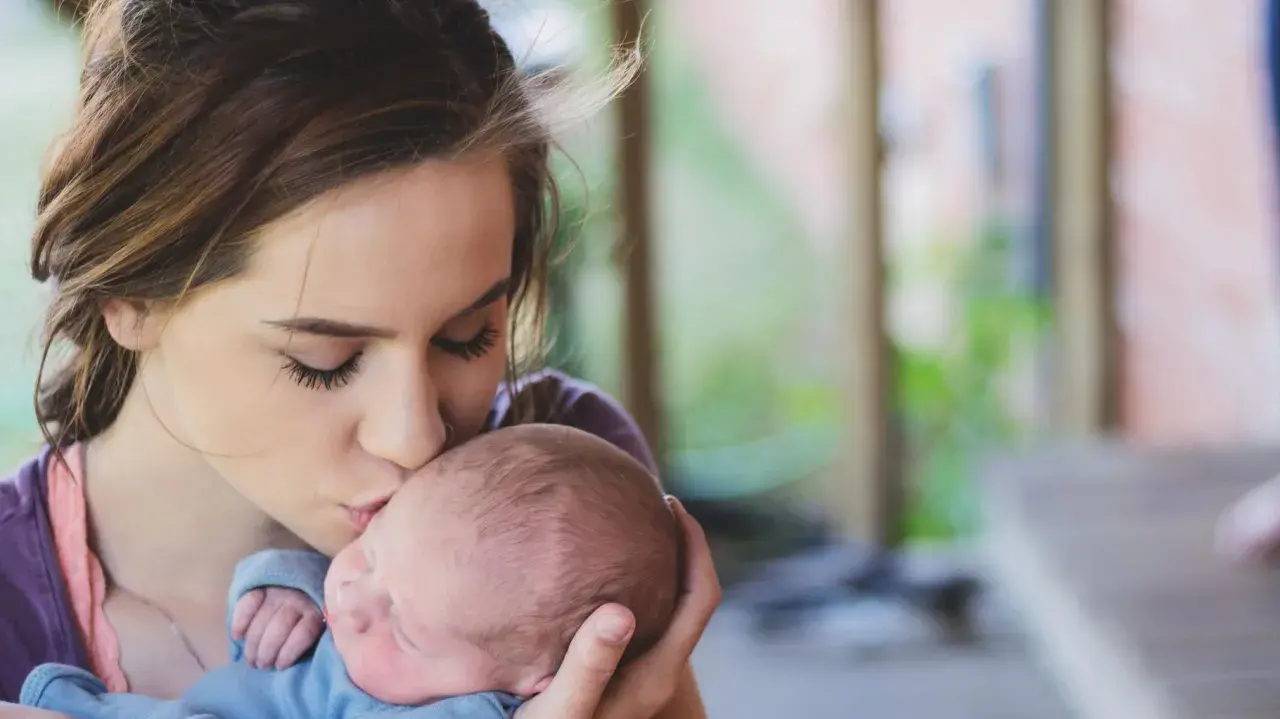 Une jeune femme, peut-être enceinte à 18 ans, embrasse tendrement son bébé.
