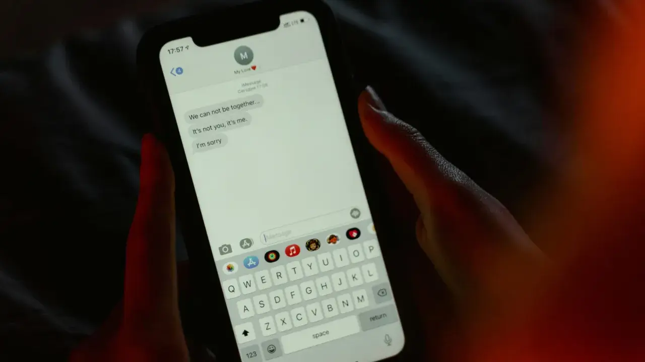 Main tenant une main sur un smartphone, affichant une conversation de rupture. Une tentative maladroite de faire rire son ex par sms.