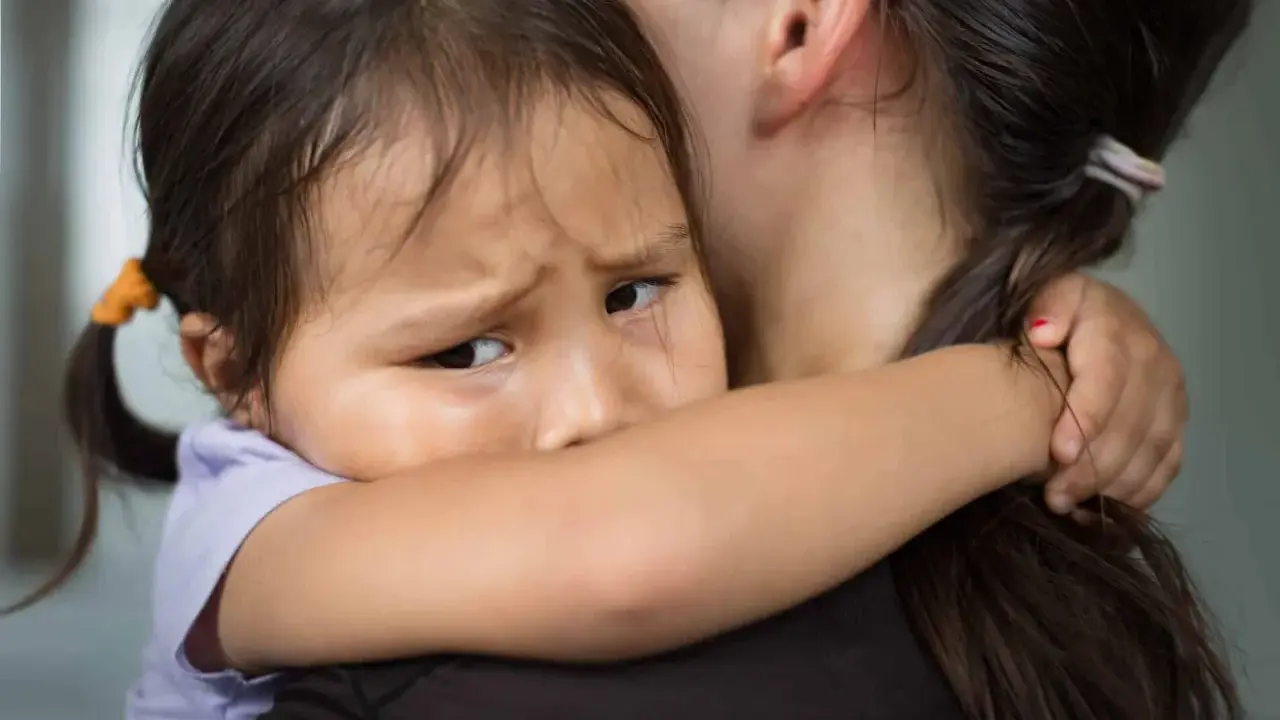 Un enfant serre sa mère, le regard plein d'angoisse de séparation.