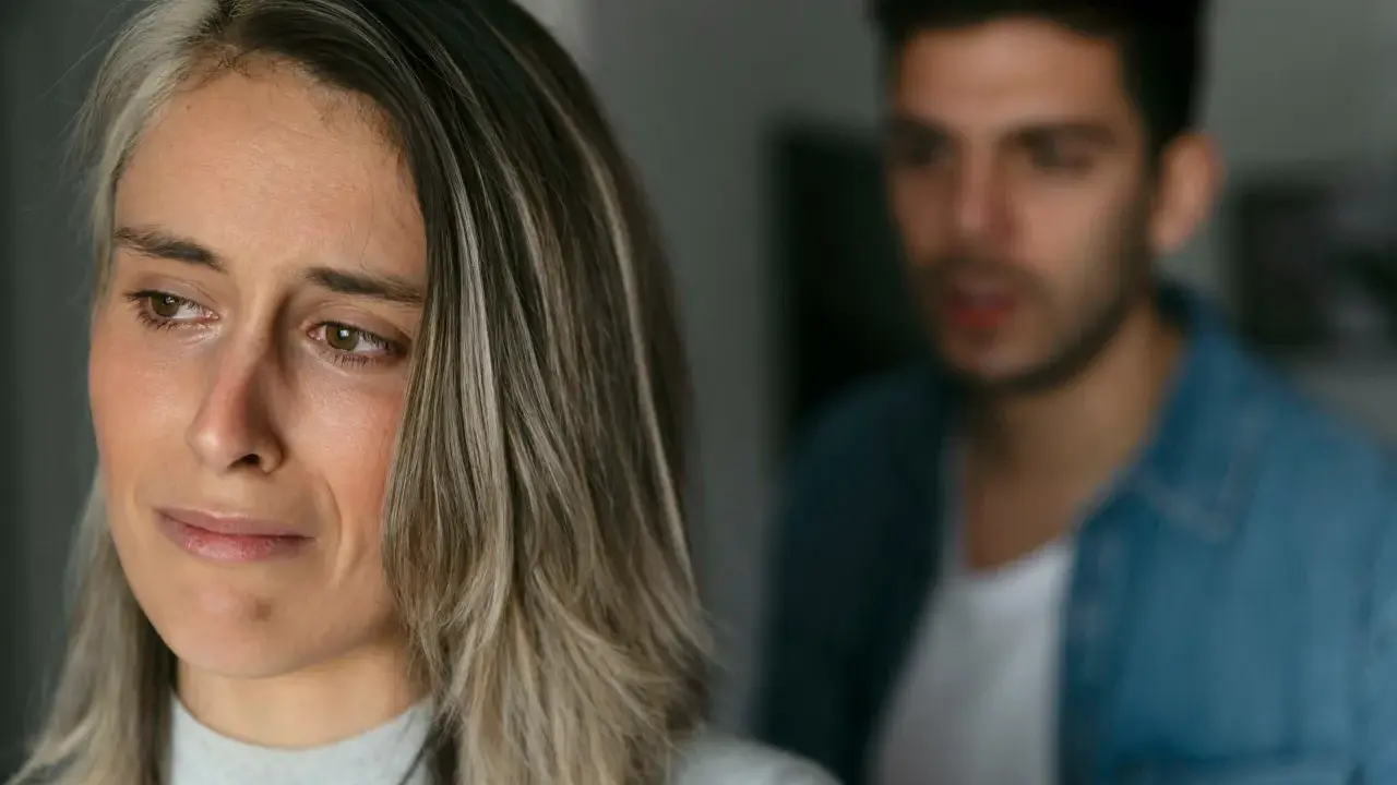 Une femme au regard triste, un homme flou en arrière-plan. Pourquoi un homme cache qu'il a une copine ? Une situation compliquée.