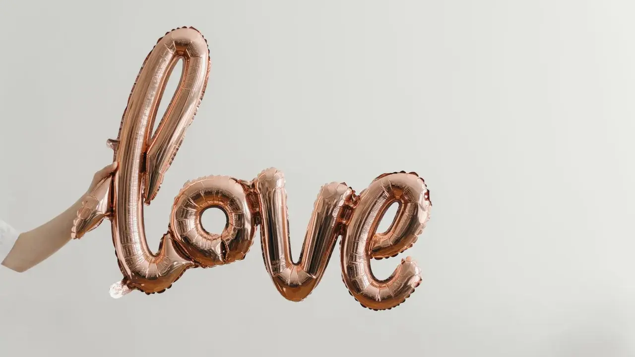 Ballon rose doré formant le mot "love", tenu par une main. Un coup de foudre sans connaître la personne, une promesse d'amour.