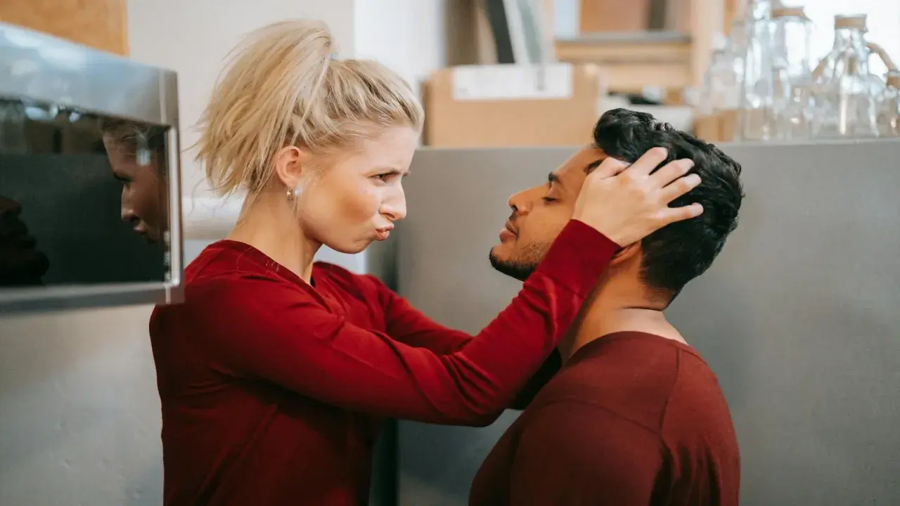 Une femme possessive ajuste la tête de son partenaire, le regardant avec une expression intense.