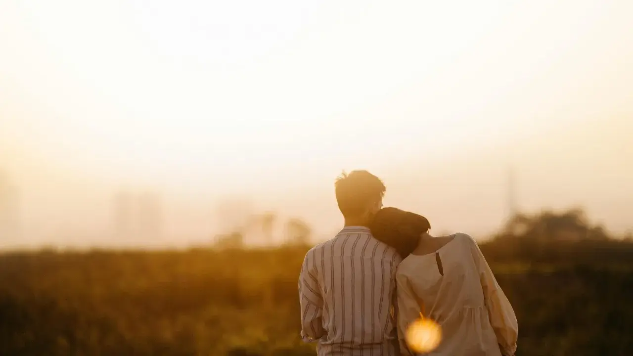 Couple assis dos à dos, la tête de la femme posée sur l'épaule de l'homme, au coucher du soleil.