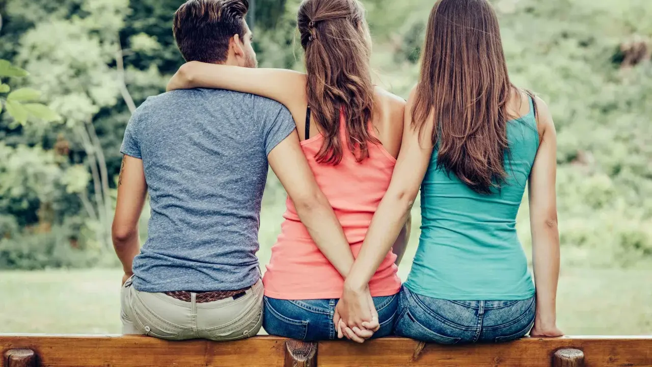Trois personnes assises sur un banc, deux femmes se tenant la main dans le dos, un homme au milieu. Une scène qui interroge sur comment faire avouer à un homme qu'il vous trompe.