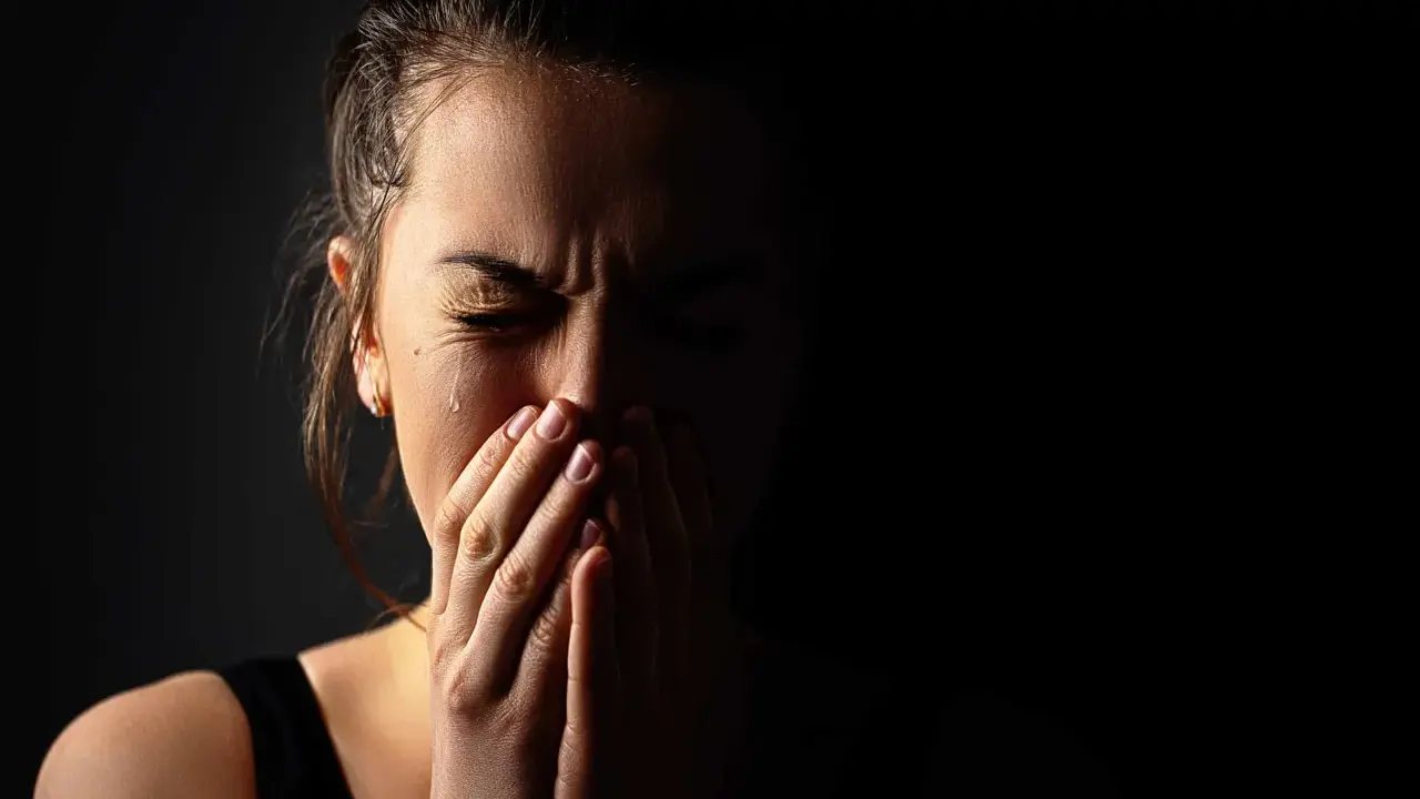 Visage d'une femme en larmes, mains sur la bouche, exprimant la détresse et les symptômes du stress post-narcissique.