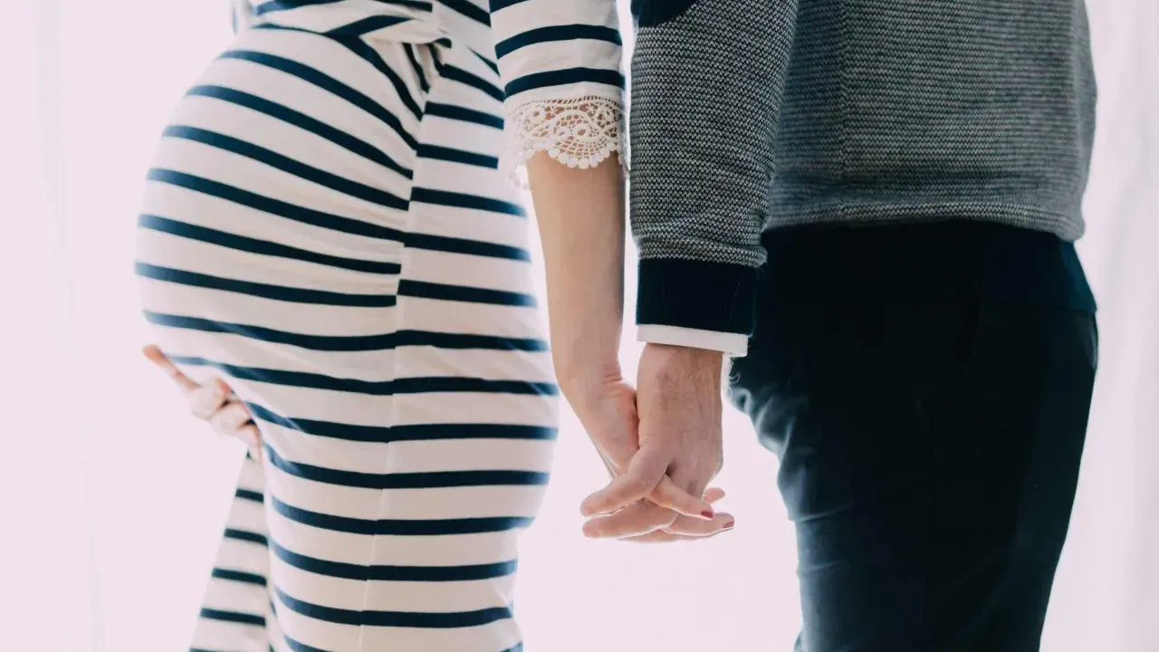 Une femme enceinte et son mari se tiennent la main. Elle porte une robe rayée, lui un pull. Il semble qu'il ne la soutienne pas pendant sa grossesse.