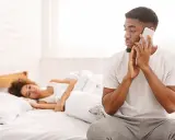 Un homme au téléphone, le regard fuyant, montre un comportement suspect alors qu'une femme dort paisiblement à côté de lui dans le lit.