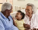 Un bébé rit aux éclats, entouré de ses grands-parents. La grand-mère, loin d'être indifférente, partage la joie de son petit-enfant.