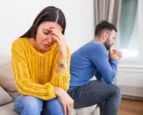 Une femme désemparée se tient la tête, son mari pensif est assis dos à elle. Elle se demande comment savoir si mon mari me trompe.