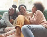 Une famille rit aux éclats sur un canapé. L'ainé de la famille, la plus grande, est au centre, entourée de ses sœurs.