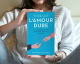 Un livre bleu intitulé "Pour que l'amour dure" est tenu par une personne. L'illustration montre deux mains se tendant l'une vers l'autre, symbolisant le début d'une histoire d'amour.