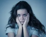 Jeune femme aux mains sur les joues, regard perdu. Elle semble passer un test de sociopathe, l'air accablé.