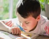 Un garçon concentré lit un livre, son doigt suivant les mots. Un test dys peut être un défi, mais sa détermination est claire.