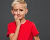 Un jeune garçon blond, le visage crispé, se tient la joue. Il semble triste, comme si mon fils se sent mal aimé.