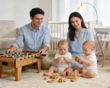 Un père joue au baby-foot pendant que la maman de jumeaux, souriante, observe ses bébés jouer avec des jouets en bois.