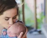 Une jeune femme, peut-être enceinte à 18 ans, embrasse tendrement son bébé.