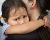 Un enfant serre sa mère, le regard plein d'angoisse de séparation.
