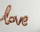 Ballon rose doré formant le mot "love", tenu par une main. Un coup de foudre sans connaître la personne, une promesse d'amour.
