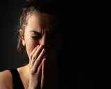 Visage d'une femme en larmes, mains sur la bouche, exprimant la détresse et les symptômes du stress post-narcissique.