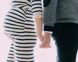 Une femme enceinte et son mari se tiennent la main. Elle porte une robe rayée, lui un pull. Il semble qu'il ne la soutienne pas pendant sa grossesse.