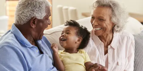 Un bébé rit aux éclats, entouré de ses grands-parents. La grand-mère, loin d'être indifférente, partage la joie de son petit-enfant.