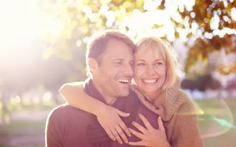Un couple souriant, peut-être traversant une crise de la cinquantaine, mais l'infidélité semble loin. Lumière dorée d'automne.
