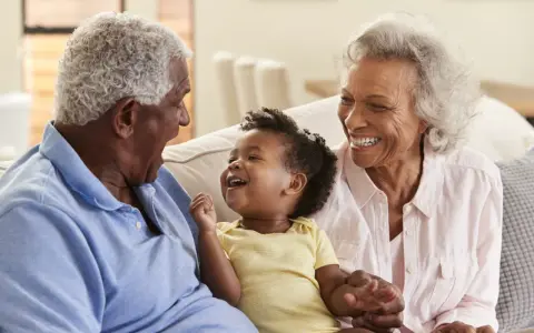 Un bébé rit aux éclats, entouré de ses grands-parents. La grand-mère, loin d'être indifférente, partage la joie de son petit-enfant.