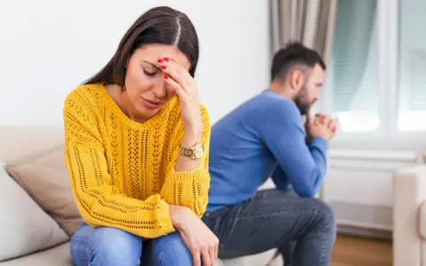 Une femme désemparée se tient la tête, son mari pensif est assis dos à elle. Elle se demande comment savoir si mon mari me trompe.