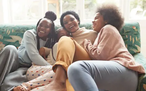Une famille rit aux éclats sur un canapé. L'ainé de la famille, la plus grande, est au centre, entourée de ses sœurs.