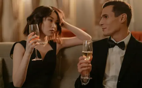 Un homme en smoking et une femme en robe noire sirotent du champagne, une scène qui pourrait inspirer sur comment séduire une fille.
