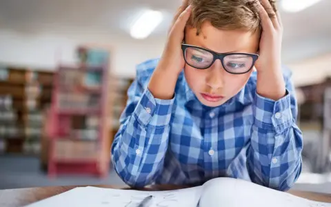 Garçon avec lunettes, mains sur la tête, visiblement en difficulté face à ses devoirs. Signes adolescent HPI, difficultés scolaires.