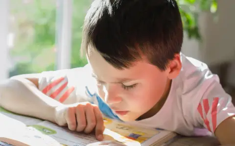 Un garçon concentré lit un livre, son doigt suivant les mots. Un test dys peut être un défi, mais sa détermination est claire.