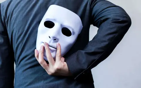 Une main cache un masque blanc derrière un costume. "Je suis narcissique, que faire ?" se demande la personne.