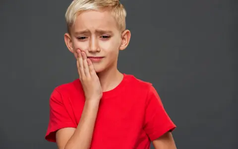 Un jeune garçon blond, le visage crispé, se tient la joue. Il semble triste, comme si mon fils se sent mal aimé.