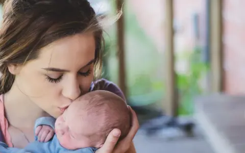 Une jeune femme, peut-être enceinte à 18 ans, embrasse tendrement son bébé.