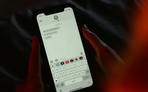 Main tenant une main sur un smartphone, affichant une conversation de rupture. Une tentative maladroite de faire rire son ex par sms.