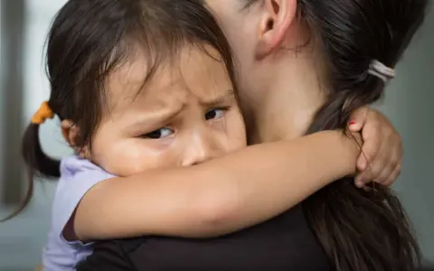 Un enfant serre sa mère, le regard plein d'angoisse de séparation.