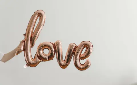 Ballon rose doré formant le mot "love", tenu par une main. Un coup de foudre sans connaître la personne, une promesse d'amour.