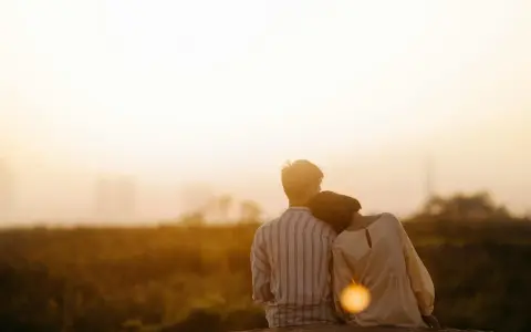 Couple assis dos à dos, la tête de la femme posée sur l'épaule de l'homme, au coucher du soleil.